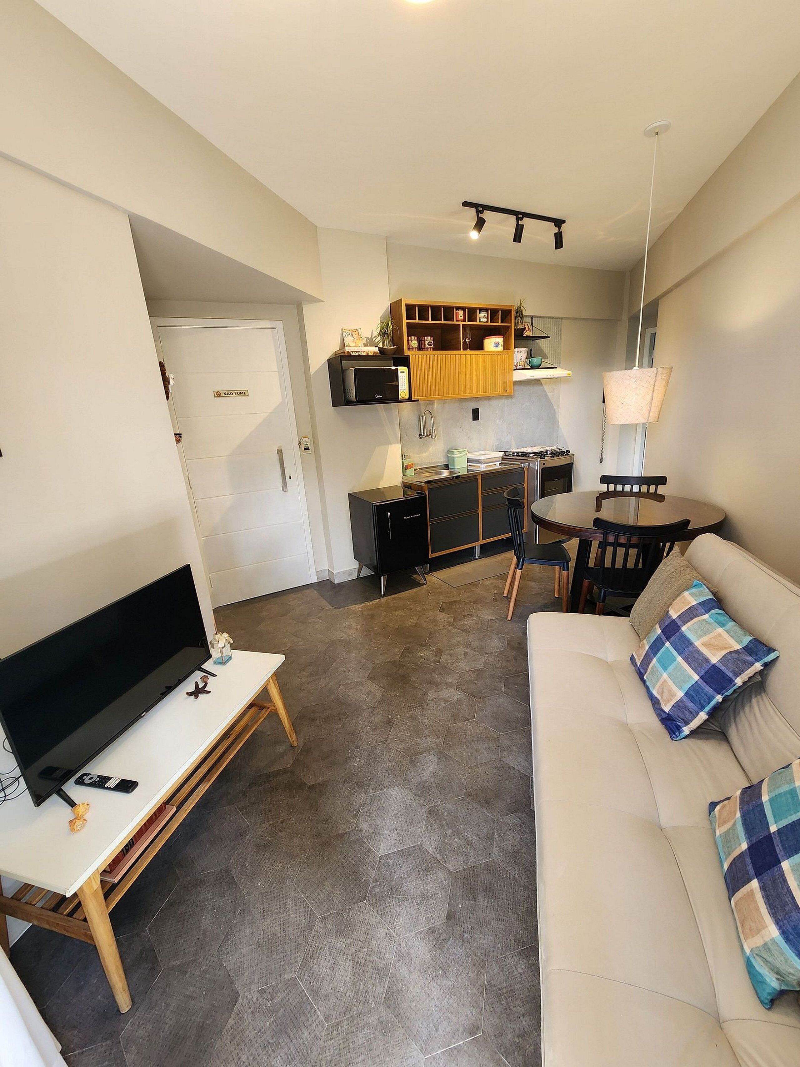 A compact living space with a sofa, a TV, a dining table, and a kitchenette.