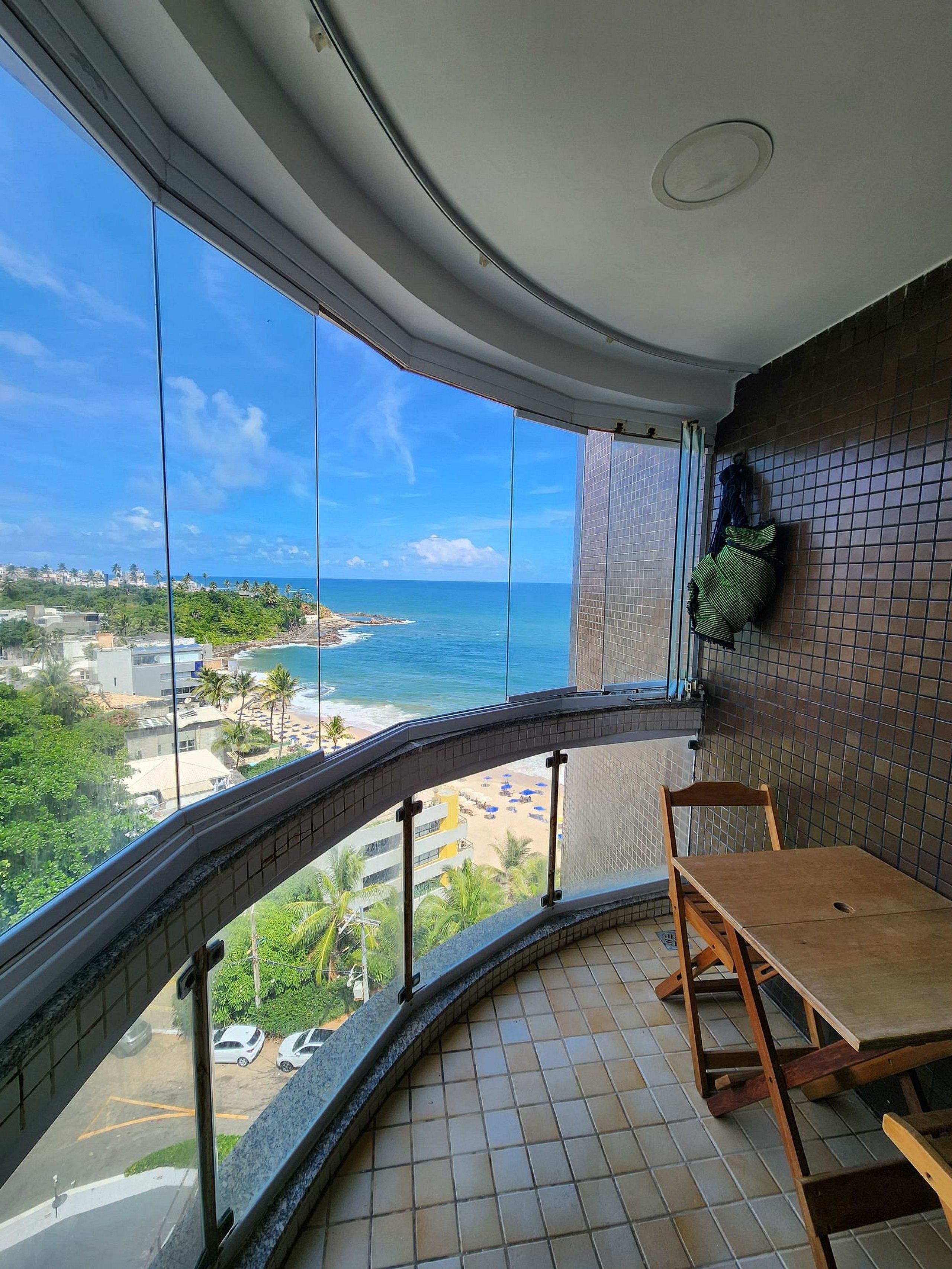 A balcony with a view of the ocean, a tiled floor, and a wooden chair.