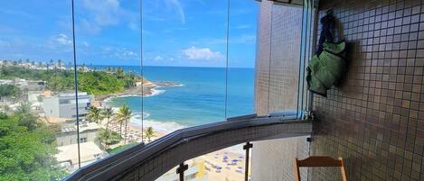 A balcony with a view of the ocean, a tiled floor, and a wooden chair.