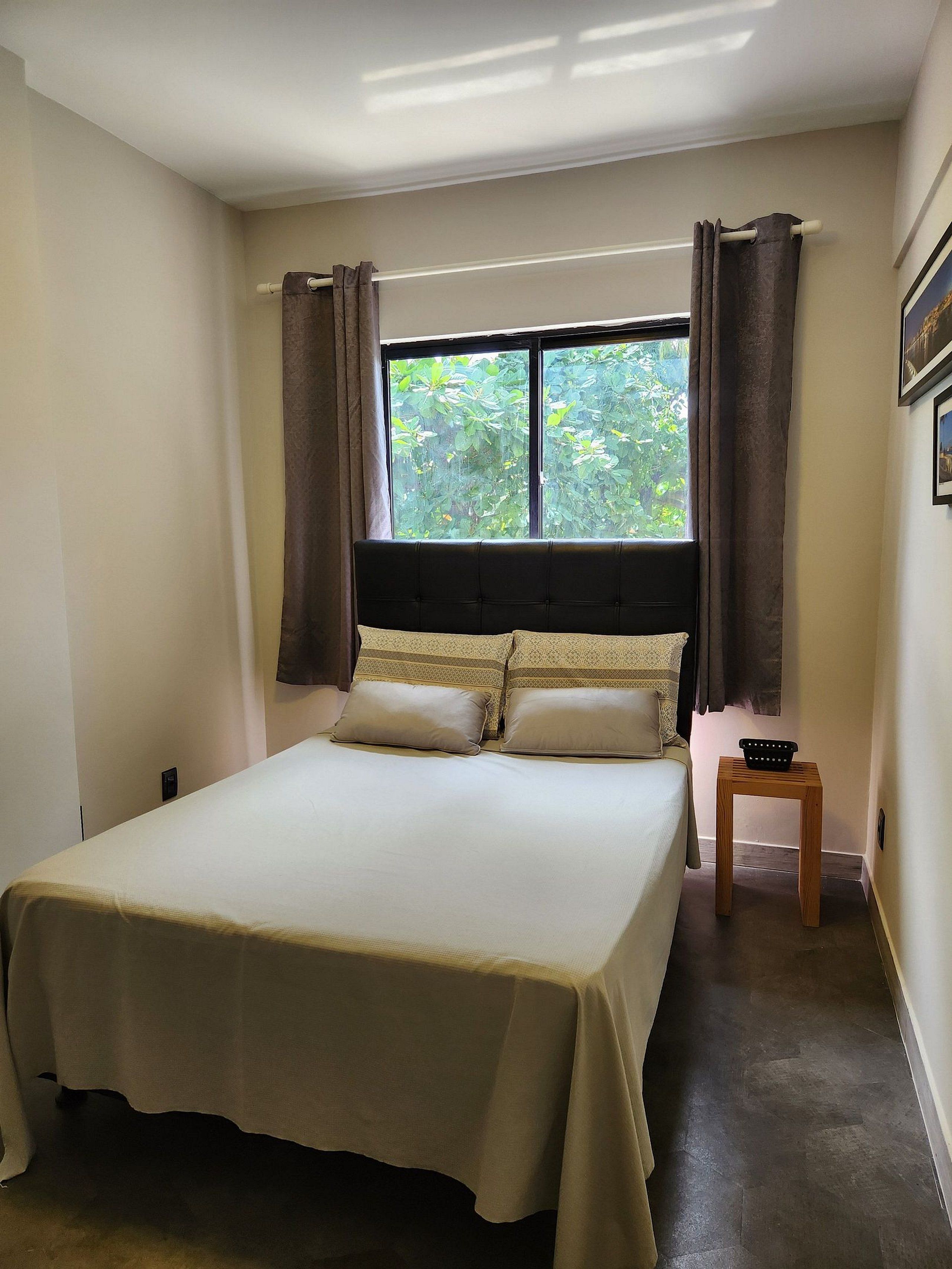 Une chambre à coucher avec un lit, des rideaux, une fenêtre et une petite table en bois.