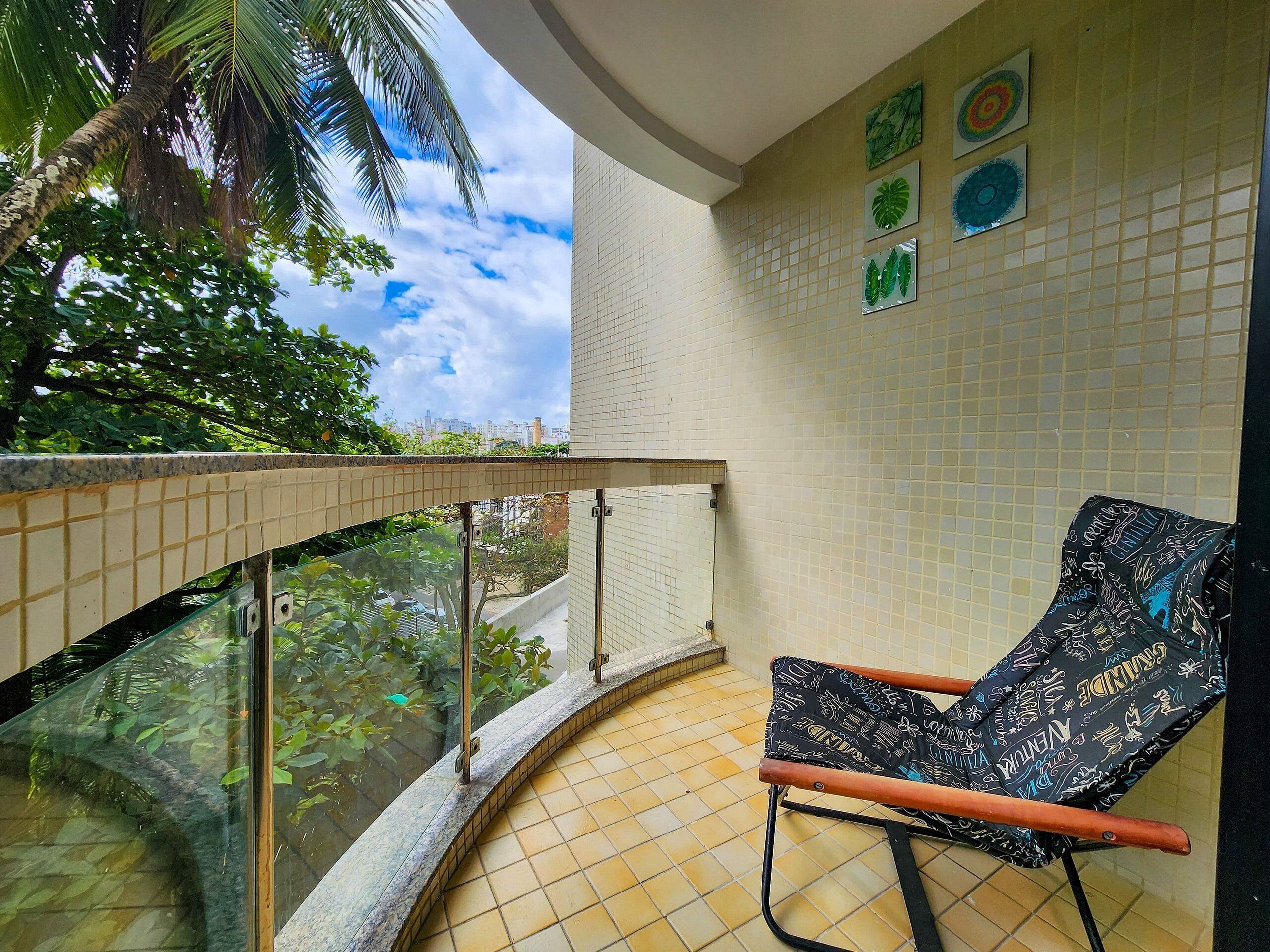 A balcony with a tiled floor, a chair, and a glass railing.