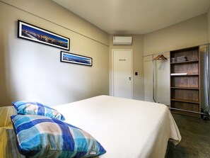 A bedroom with a bed, two framed pictures, a wardrobe, and a clothes rack. - Sol Nascente (Salvador)