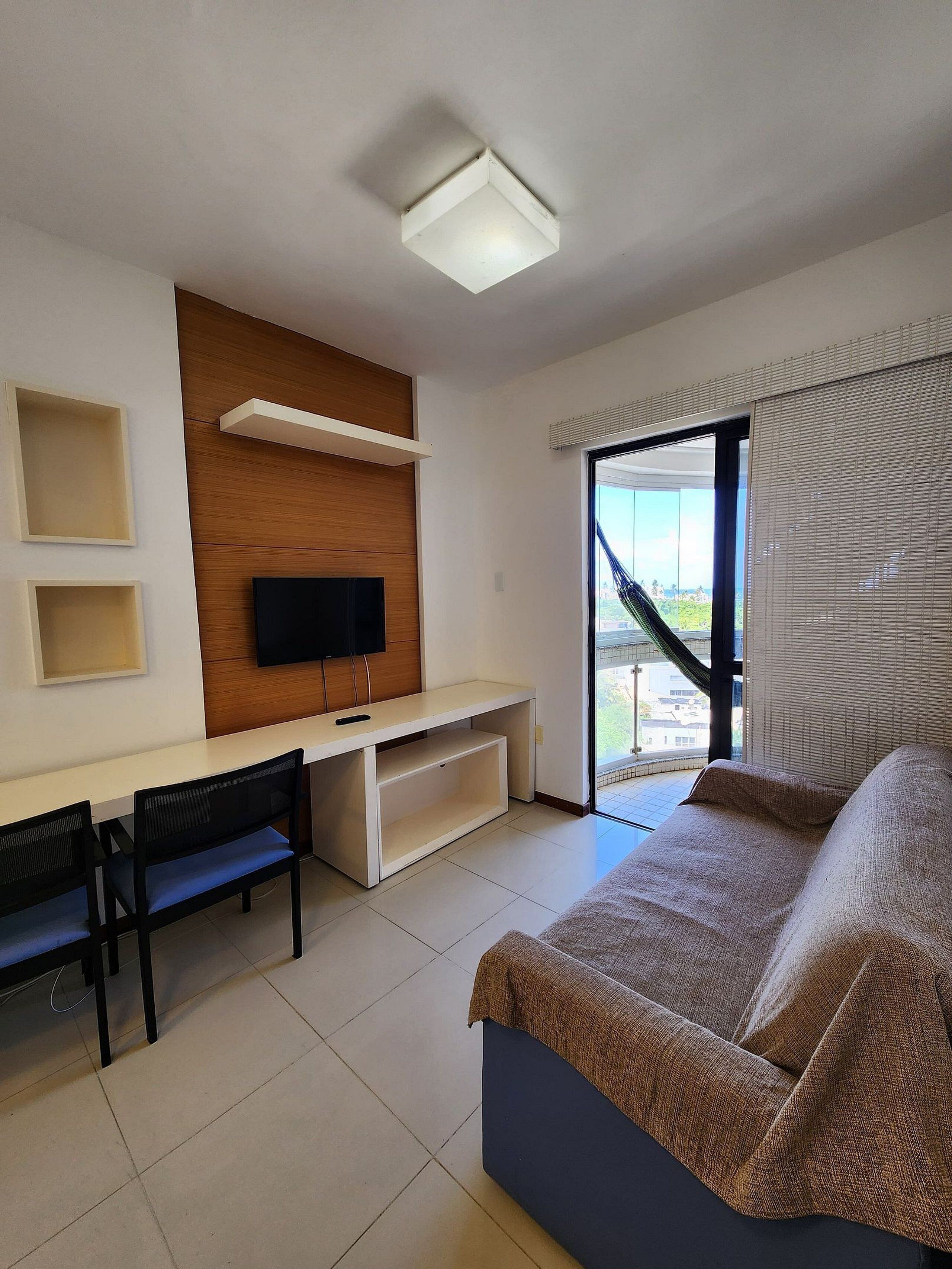 Une chambre d’hôtel avec un lit, un bureau avec une télévision, une chaise et une fenêtre avec des stores.