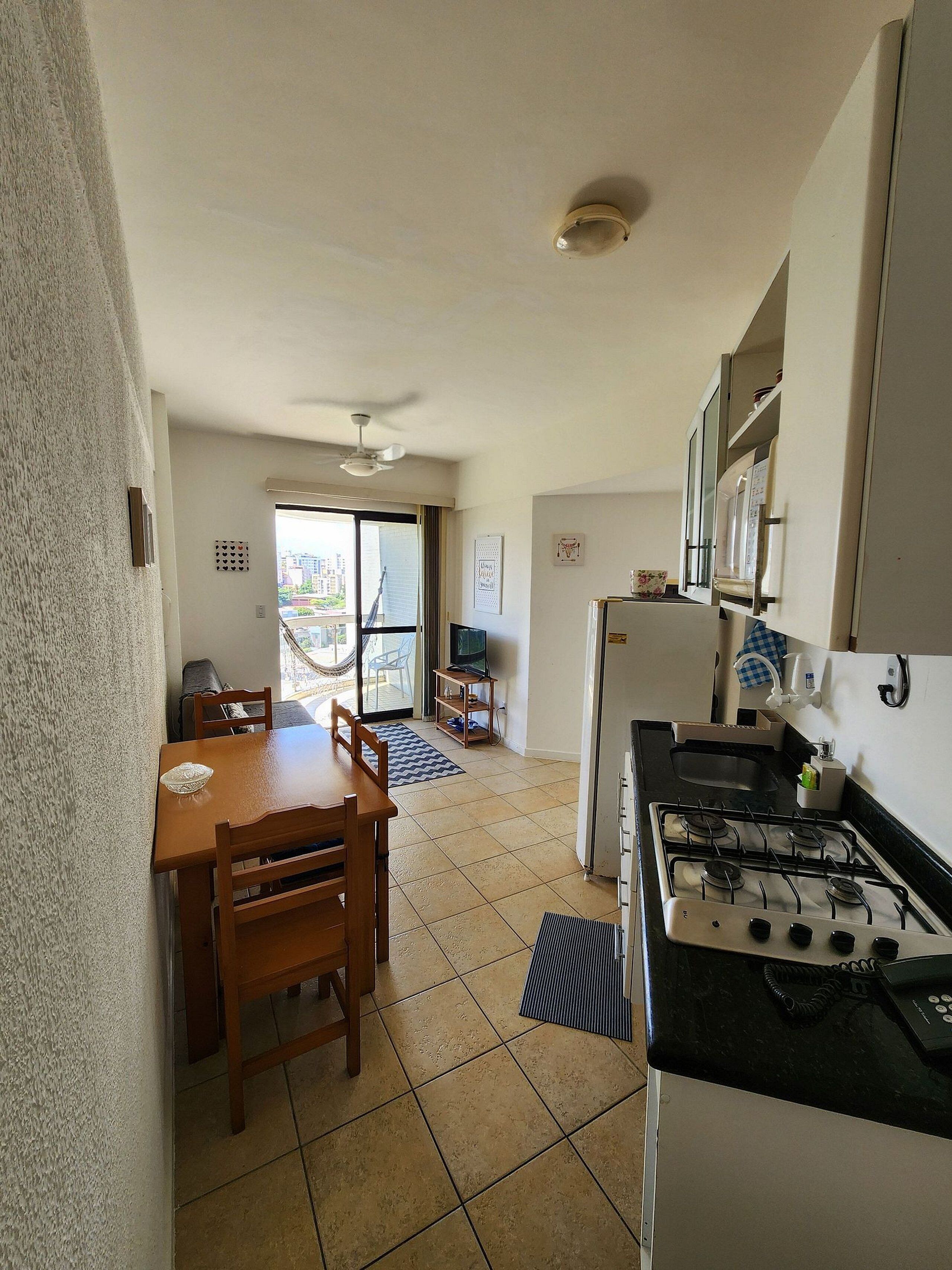 A compact kitchen with a gas stove, a dining table with chairs, a TV, and a view of the outside through a sliding door.