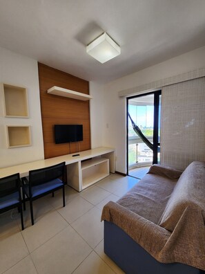 A hotel room with a bed, a desk with a TV, a chair, and a window with blinds. - Sol Nascente (Salvador)