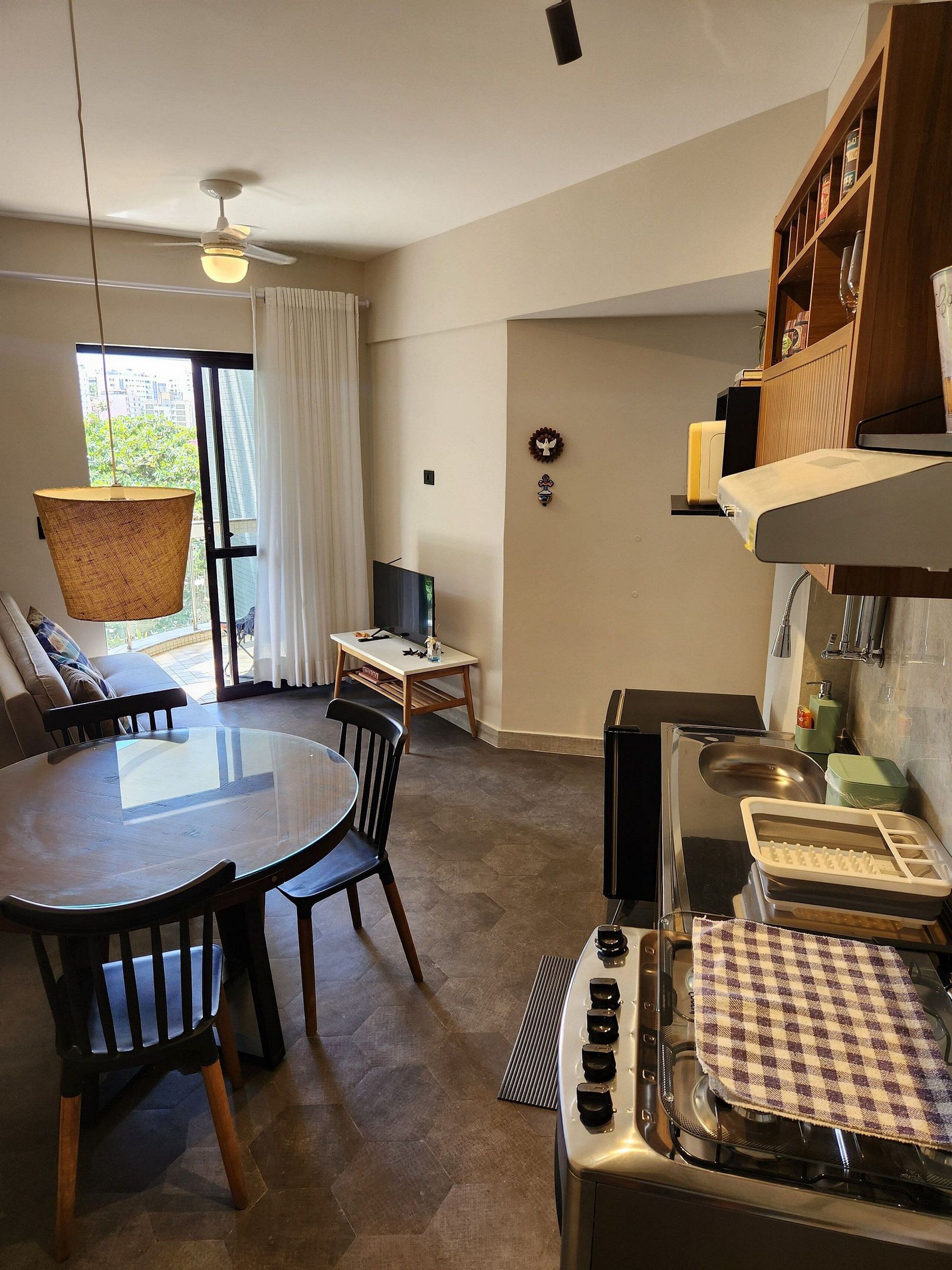 Une cuisine moderne équipée d’une cuisinière à gaz, d’une table à manger avec des chaises, d’un luminaire suspendu et offrant une vue sur le paysage urbain à travers une grande fenêtre.