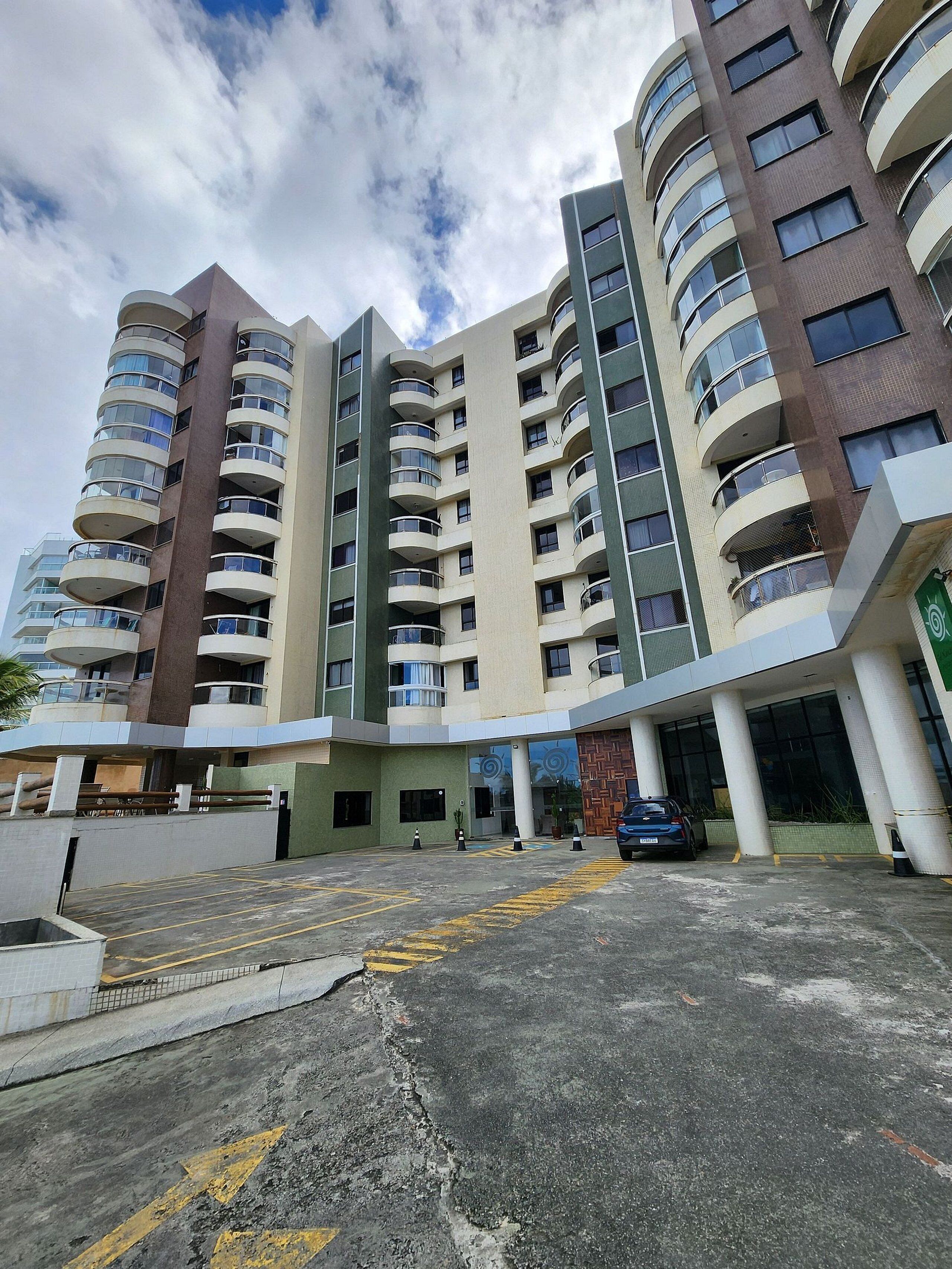 A multi-story residential building with balconies, a parking area, and a gated entrance.