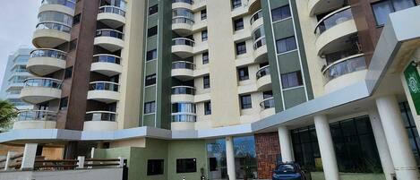 A multi-story residential building with balconies, a parking area, and a gated entrance.