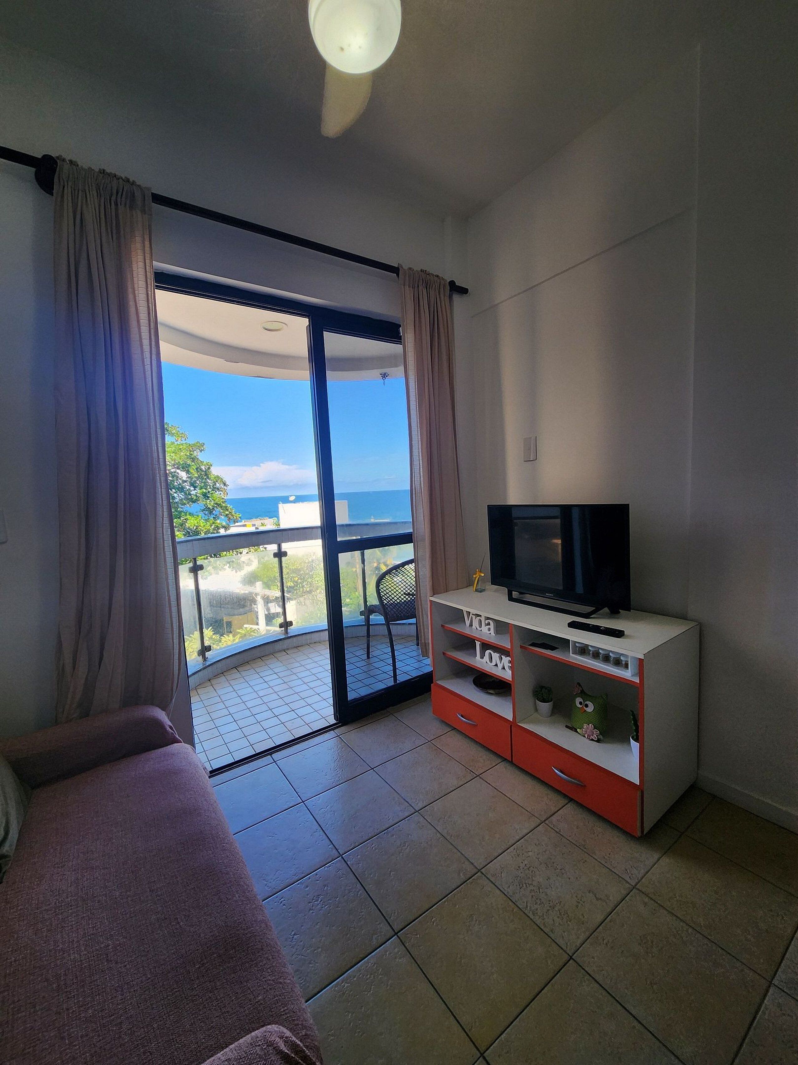 Una stanza con balcone, televisione su un mobile e vista sul mare.