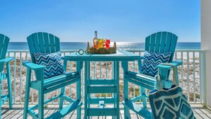 Um deck turquesa com duas cadeiras e uma mesa, com vista para uma praia.