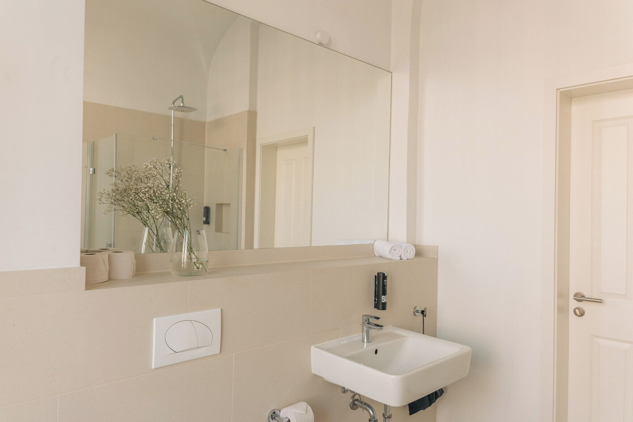 A bathroom with a large mirror, a sink, and a shower.