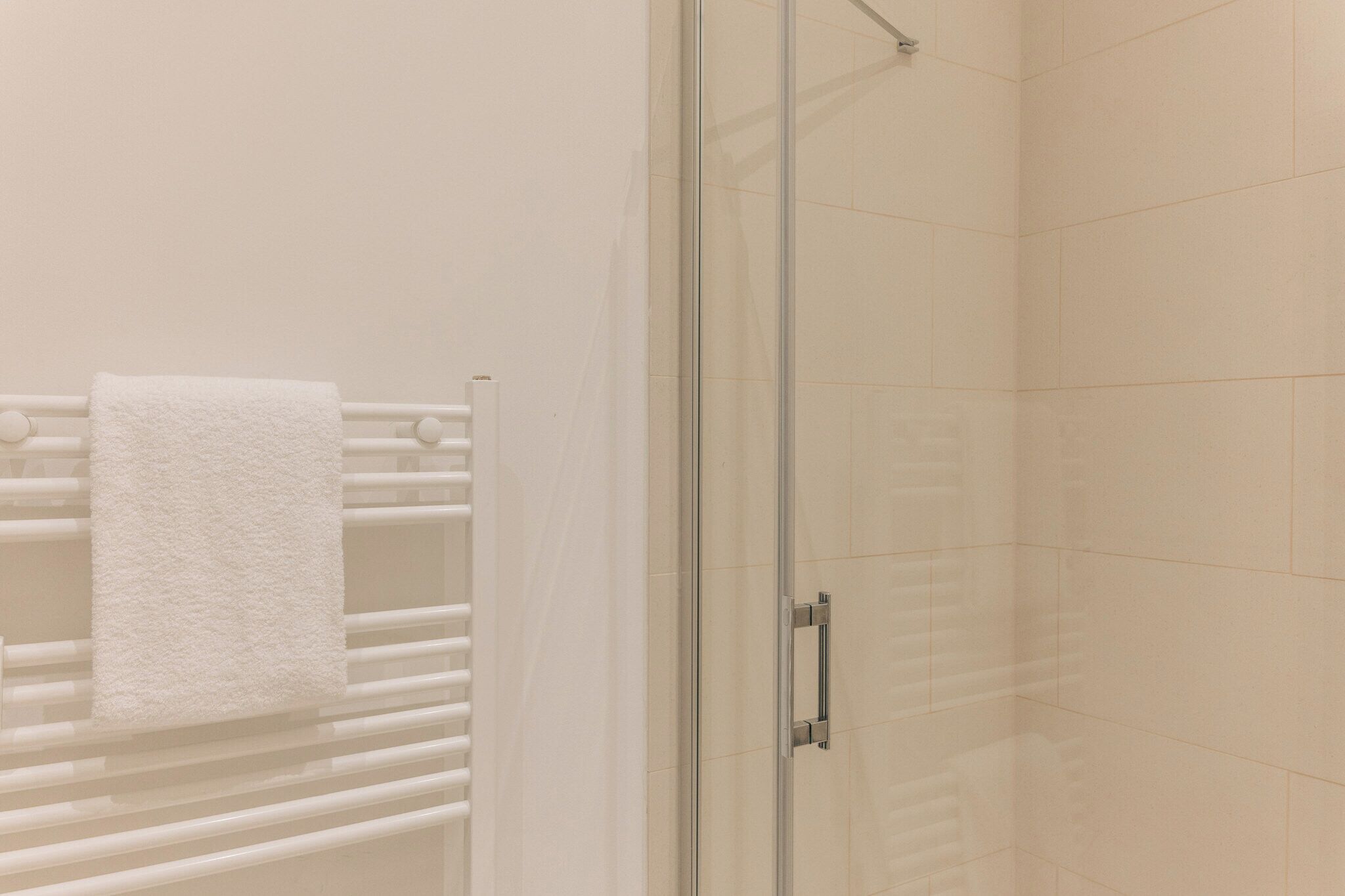 A glass-enclosed shower with a white towel hanging on a rack.