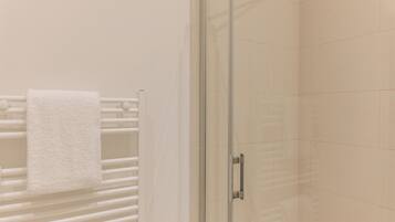 A glass-enclosed shower with a white towel hanging on a rack.