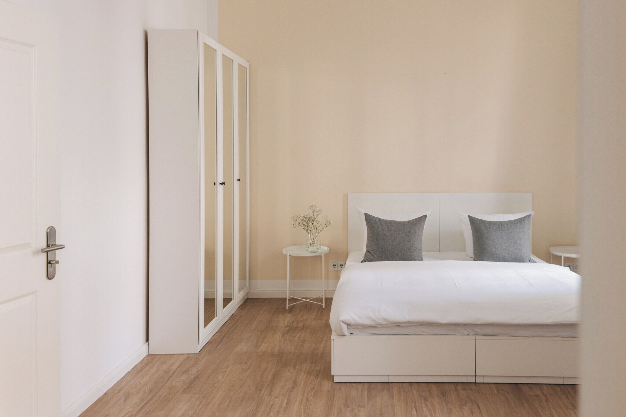 Une chambre à coucher comprenant un lit, une table de chevet, une petite table avec un vase et une armoire.