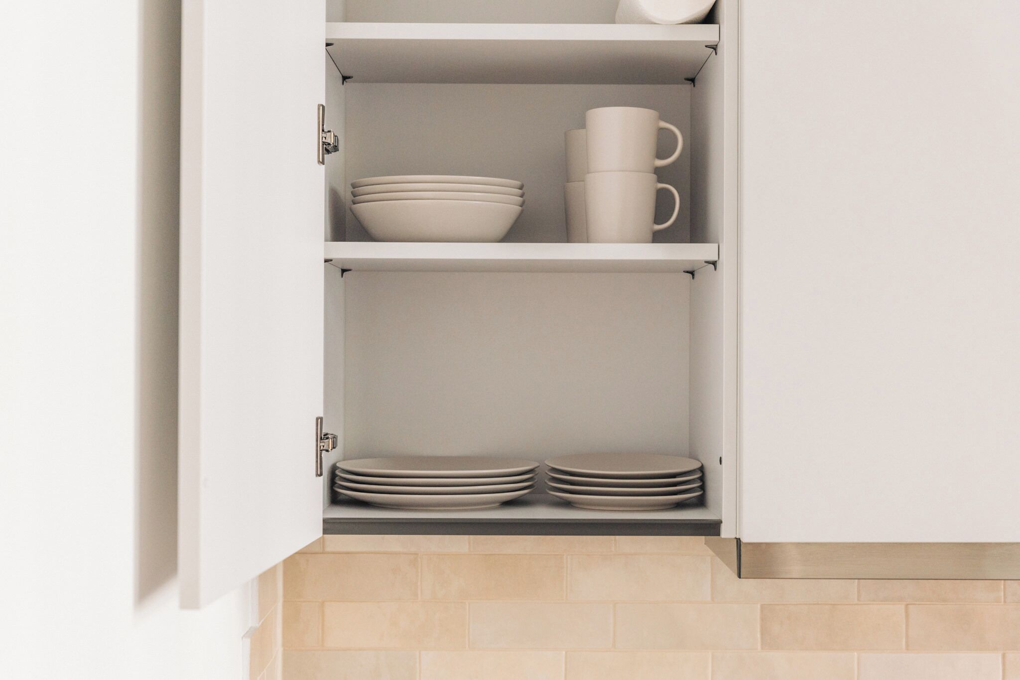 A kitchen cabinet with shelves holding bowls, plates, and a mug.