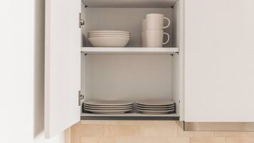 A kitchen cabinet with shelves holding bowls, plates, and a mug.