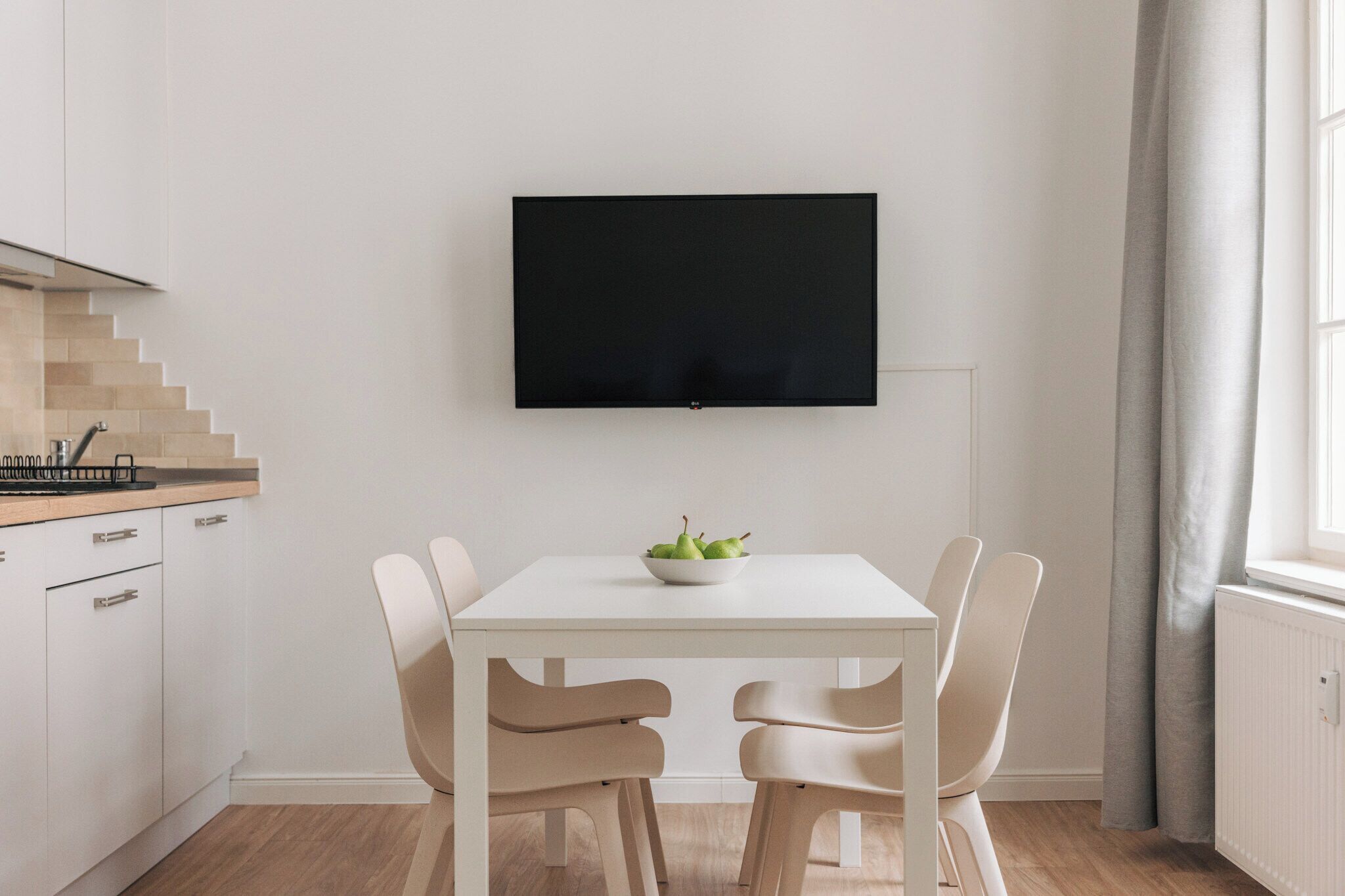Ett modernt kök med ett vitt bord, två stolar och en platt-TV som är monterad på väggen.