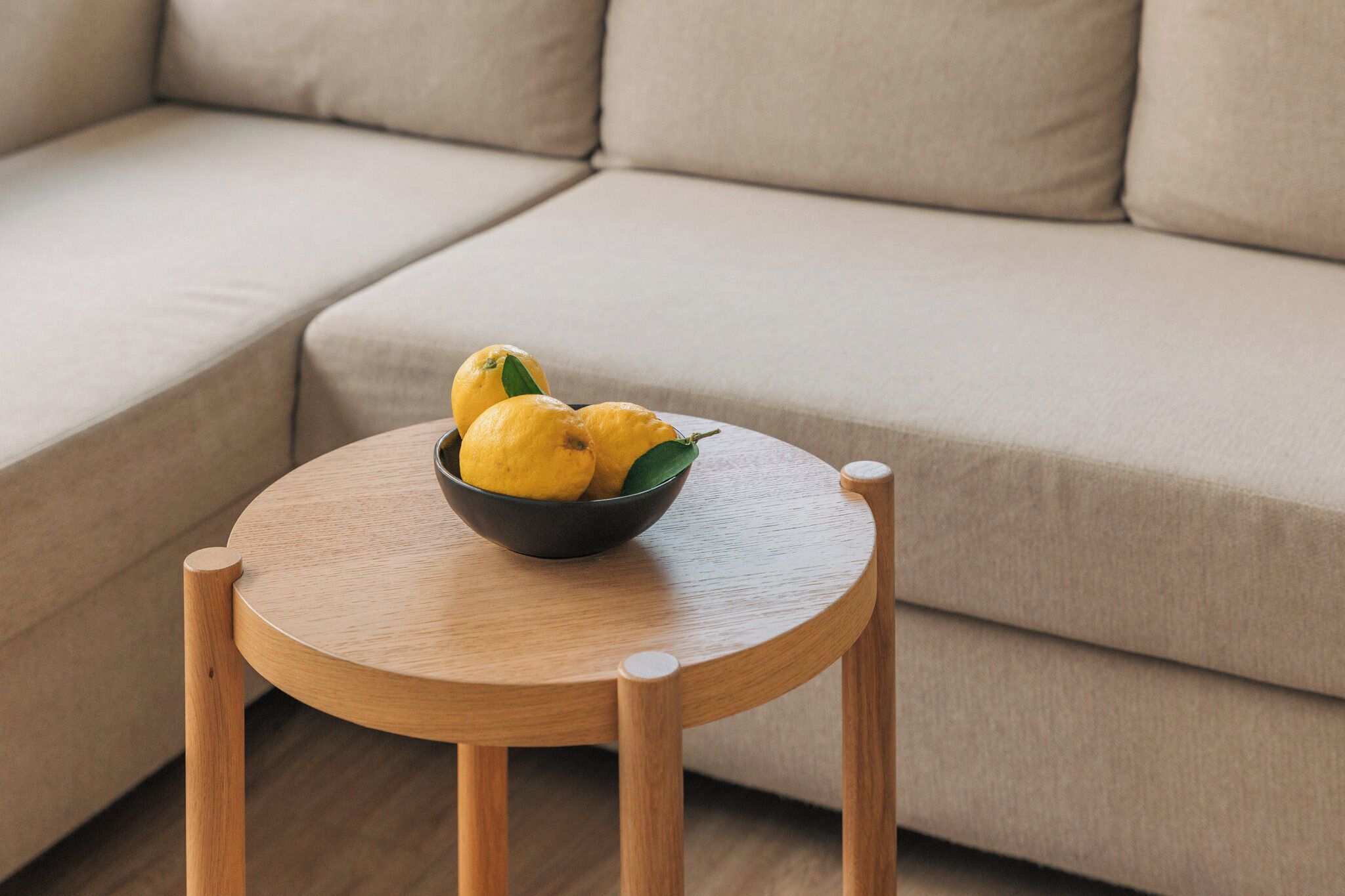 A round wooden table with a bowl of lemons on a beige sofa.