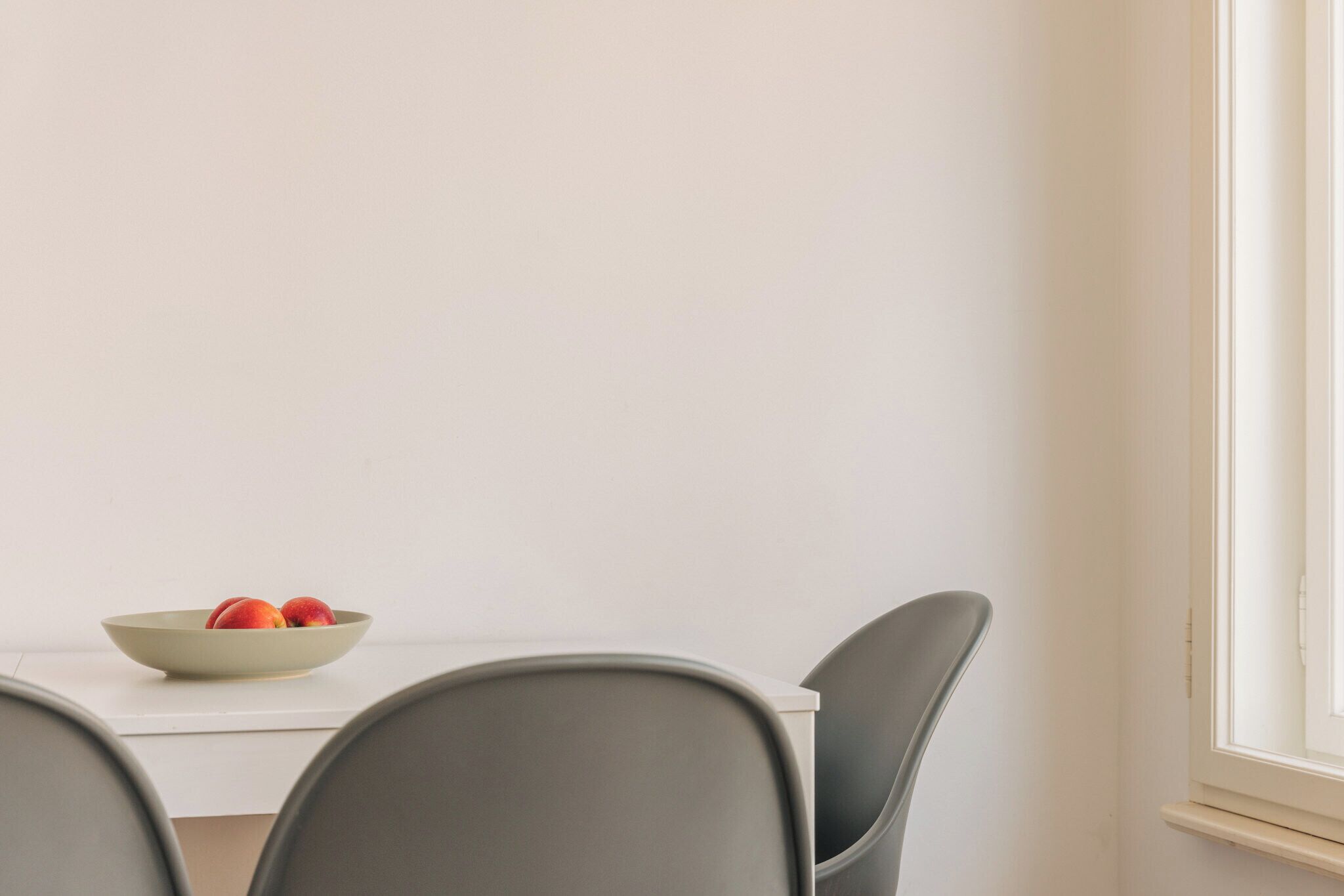 Un comedor con una mesa blanca, dos sillas grises y un frutero sobre la mesa.