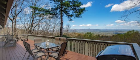 A wooden deck with outdoor furniture, a grill, and a scenic view of mountains and trees.