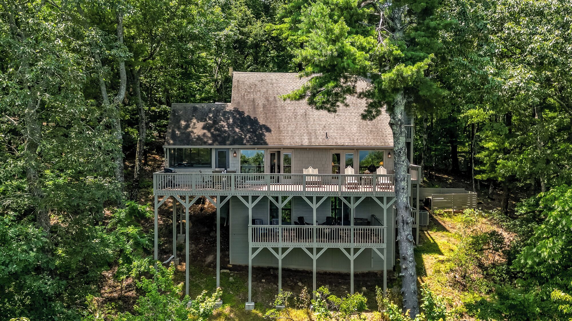 A two-story cabin with a balcony, surrounded by dense forest.