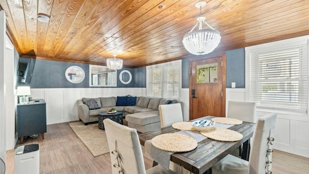 A cozy living room with a wooden ceiling, a gray sofa, a dining table with placemats, and a chandelier. - Pool, Firepit, Walk To Beach- A Haven By The Sea (North Myrtle Beach)