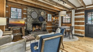 A rustic cabin interior with a stone fireplace, wooden walls, and a cozy seating area.
