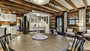 A rustic interior with exposed wooden beams, a central round table, and a cozy seating area.