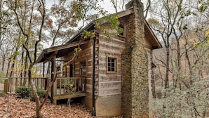 A rustic cabin with a stone chimney, wooden exterior, and a porch.