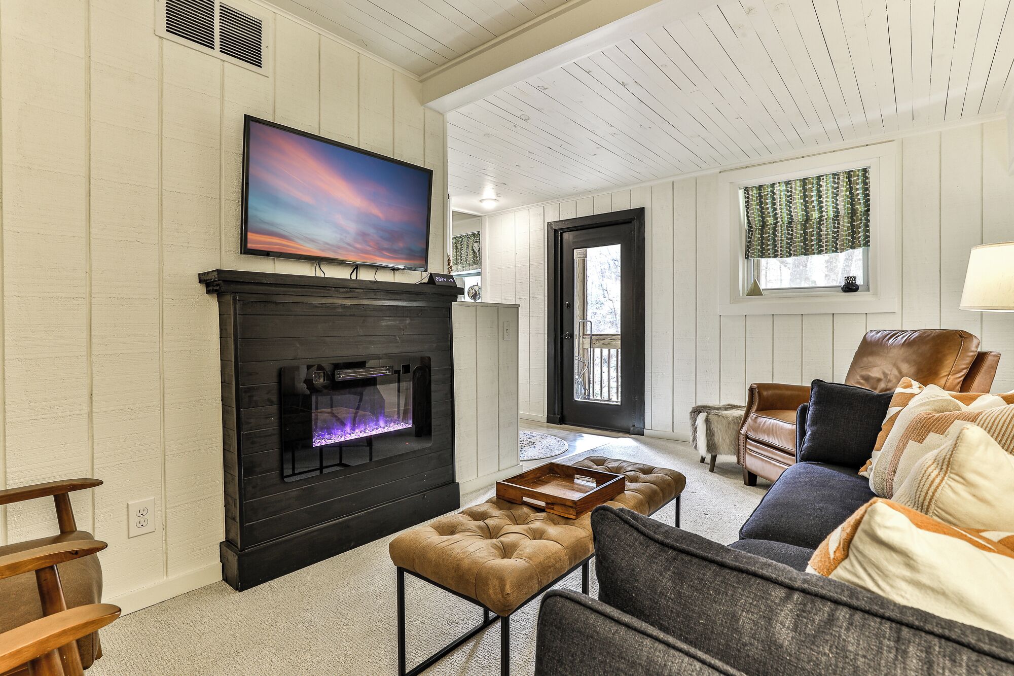 Una sala de estar con chimenea, un televisor montado encima y un sofá con cojines.