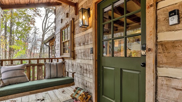 A rustic cabin with a green door, a porch with a bench, and a wooden exterior.