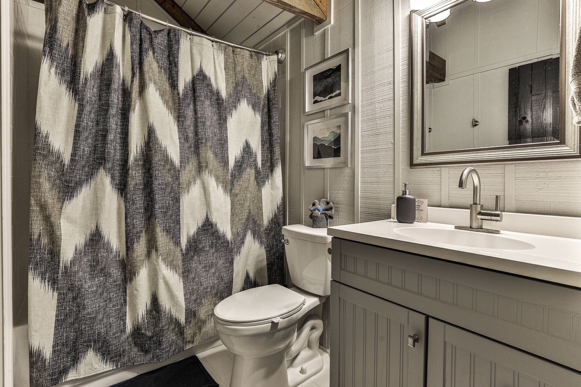A bathroom with a shower curtain, toilet, sink, and mirror.