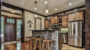 A kitchen with wooden bar stools, a stone island, stainless steel appliances, and wooden cabinets. - Elk Horn - Big Canoe GA (Big Canoe)