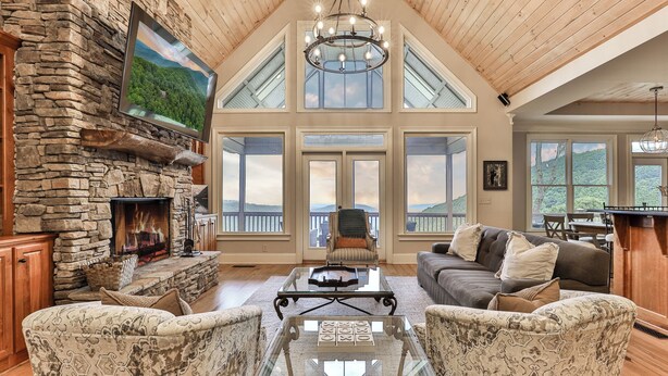 A spacious living room with a stone fireplace, large windows, and a high ceiling. - Endless Sky Lodge - Big Canoe GA (Big Canoe)
