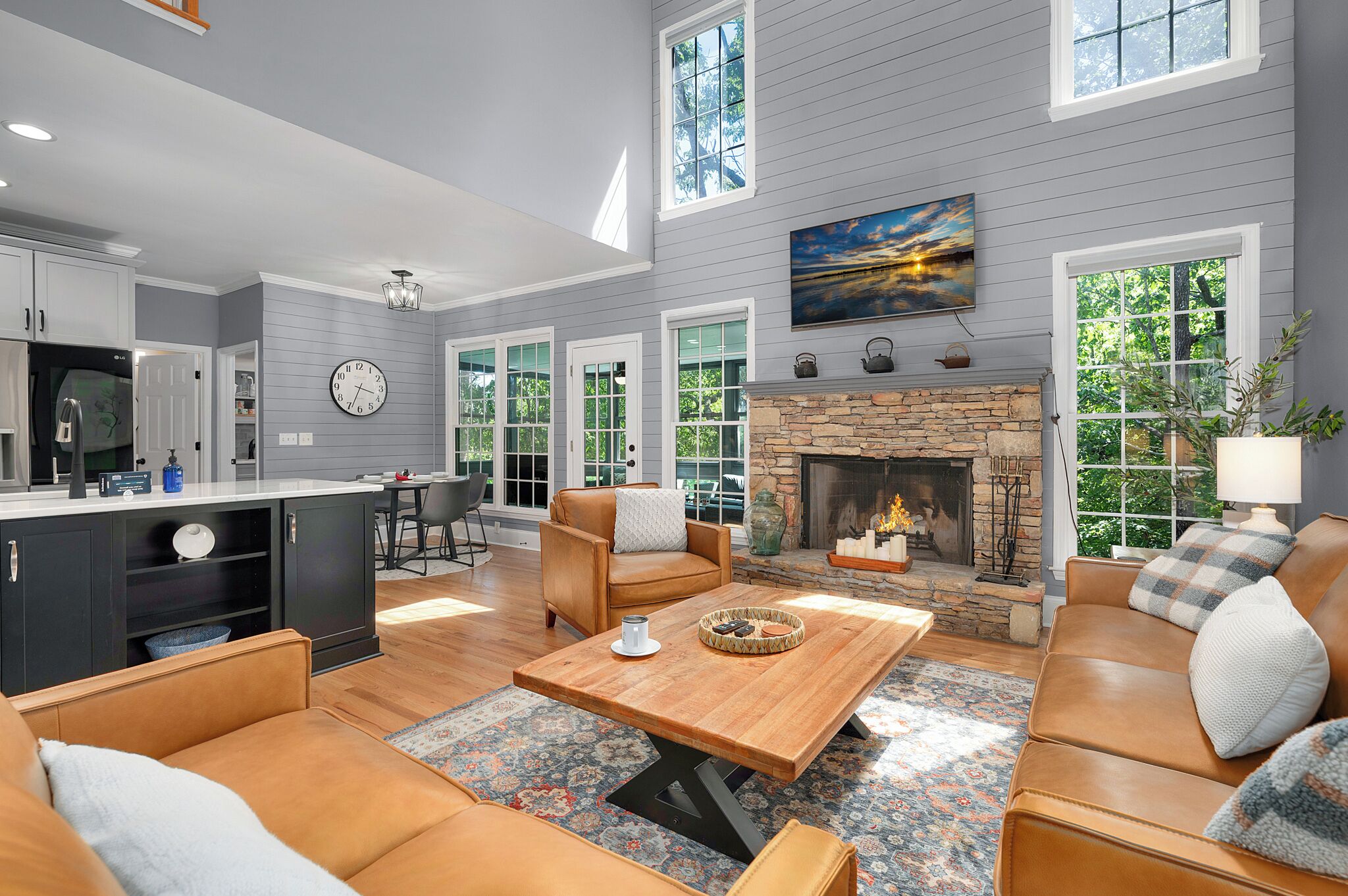 A spacious living room with a fireplace, leather sofas, a coffee table, and large windows offering views of the outdoors.