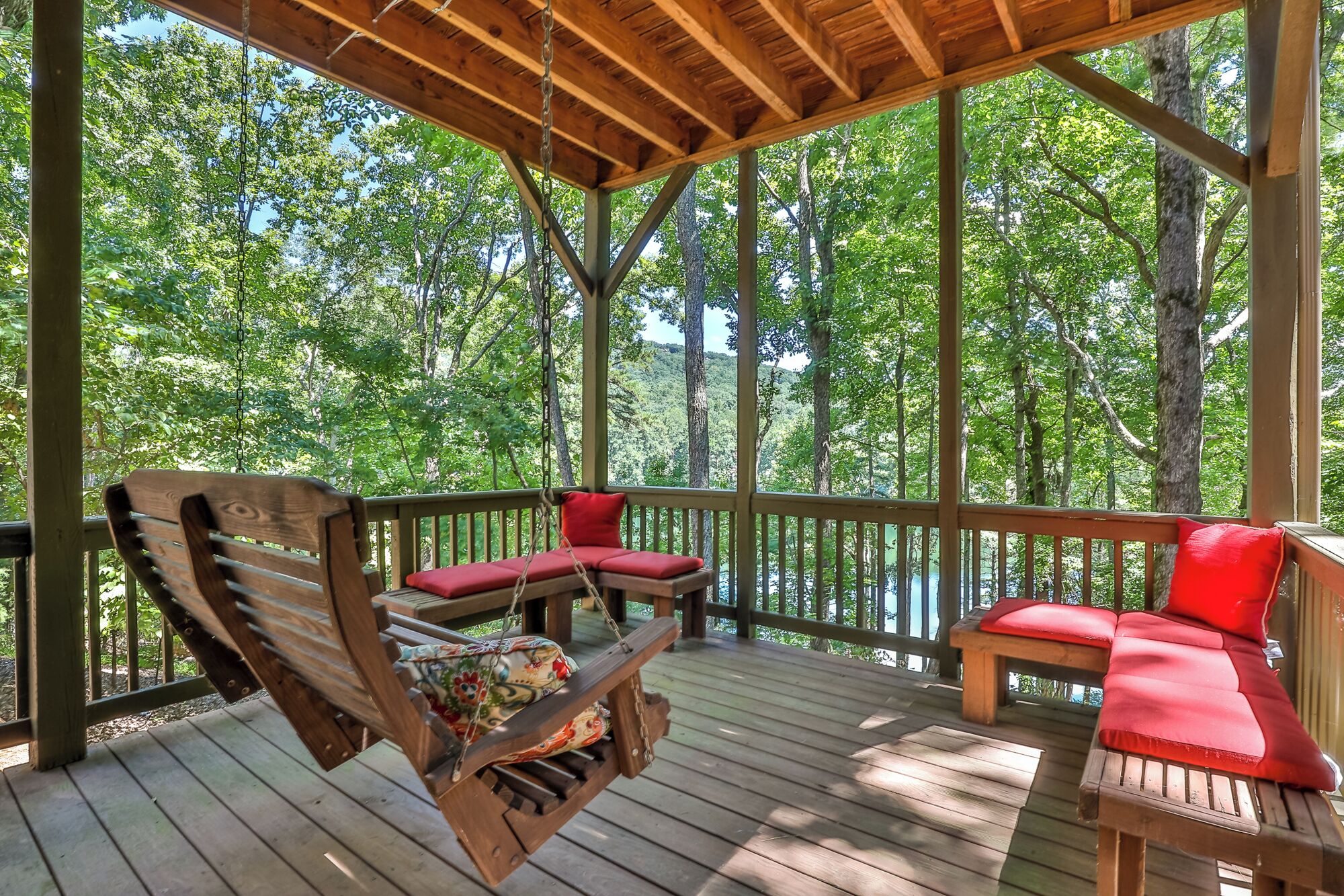 A wooden deck with a swing chair and two cushioned benches, surrounded by trees.
