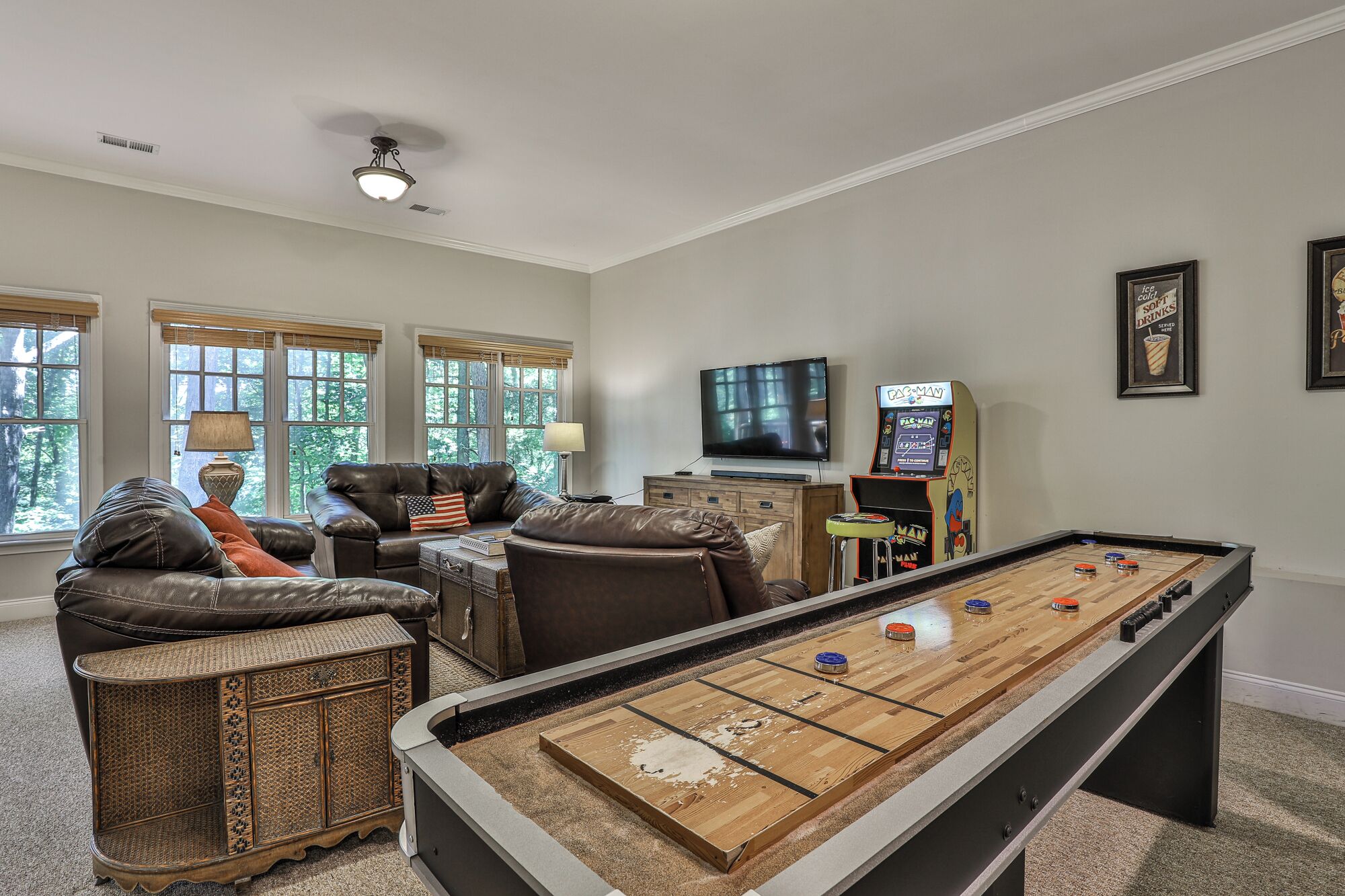 A living room with a pool table, leather sofas, a television, and a Pac-Man arcade machine.