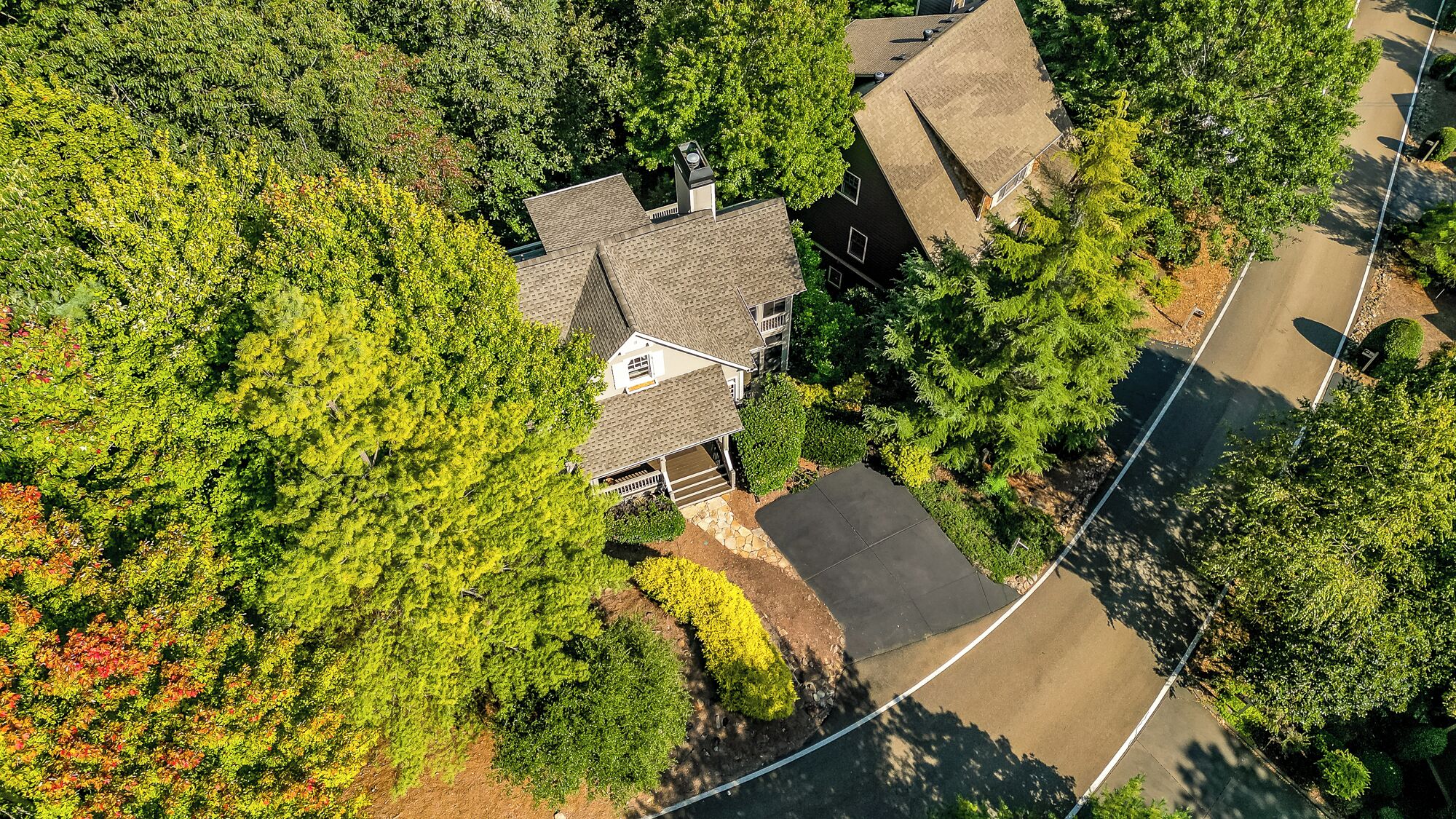 An aerial view of a residential area with a house featuring a sloped roof, a garage, and a driveway.
