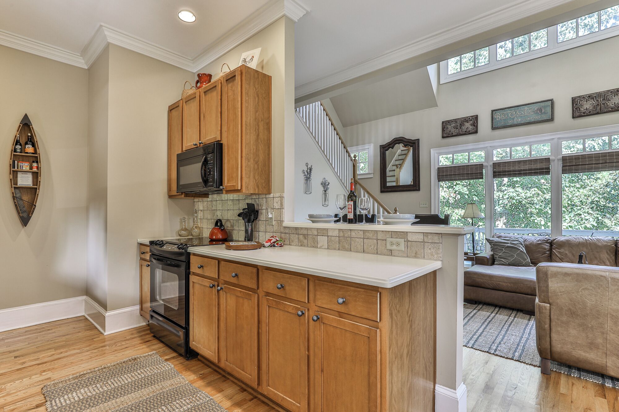 A kitchen with wooden cabinets, a microwave, and a stove. There is a dining area with a sofa and a window with a view of trees.