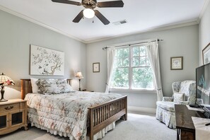 Une chambre à coucher avec un lit, une table de chevet, une lampe, une fenêtre et un ventilateur de plafond.
