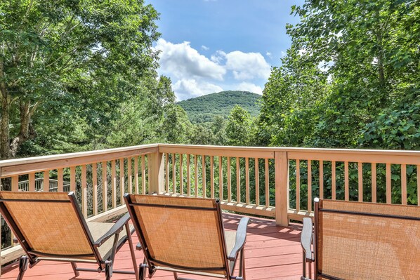 Une terrasse en bois, dotée de chaises en osier, qui offre une vue sur une colline boisée.