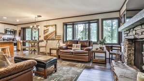 Un salon chaleureux avec une cheminée, des meubles en cuir, un coin repas et de grandes fenêtres.