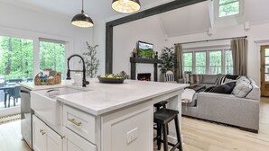 A modern kitchen with a central island, a dining area with a view of the forest, and a cozy living room with a fireplace.