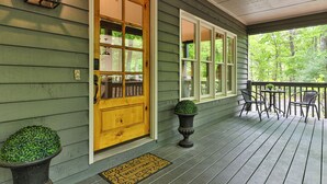 A wooden porch with a door, a small table with chairs, and a potted plant.