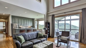 A spacious living room with a leather sofa and ottoman, a wooden coffee table, and a view of a kitchen and balcony. - Southern Views - Big Canoe GA (Big Canoe)