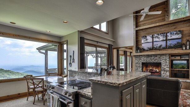 A modern kitchen with a stone fireplace, large windows offering scenic views, and a dining area with a view. - Southern Views - Big Canoe GA (Big Canoe)