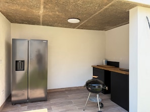 Une cuisine équipée d’un réfrigérateur en acier inoxydable, d’un four encastré et d’un barbecue mobile.