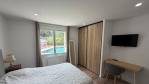 Une chambre avec un lit, un bureau, une télévision, une fenêtre donnant sur une piscine et une porte coulissante.