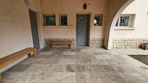 Une cour dallée de pierres, avec un banc, une porte et une petite fenêtre grillagée.