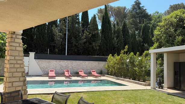 Un jardin avec une piscine, des chaises longues, une table avec des chaises et un patio couvert.